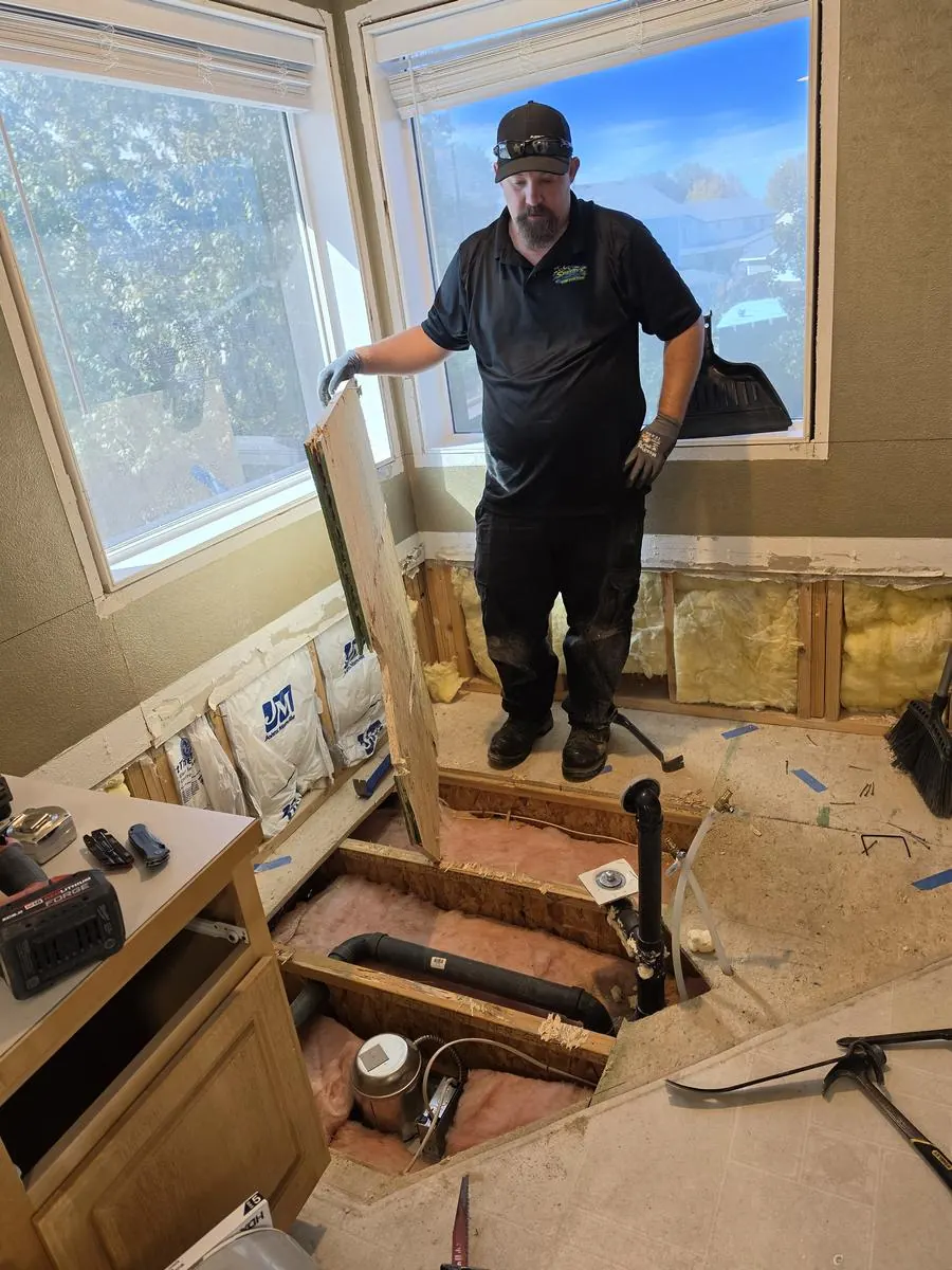 Gutted bathroom corner with the old tub removed and subfloor exposed