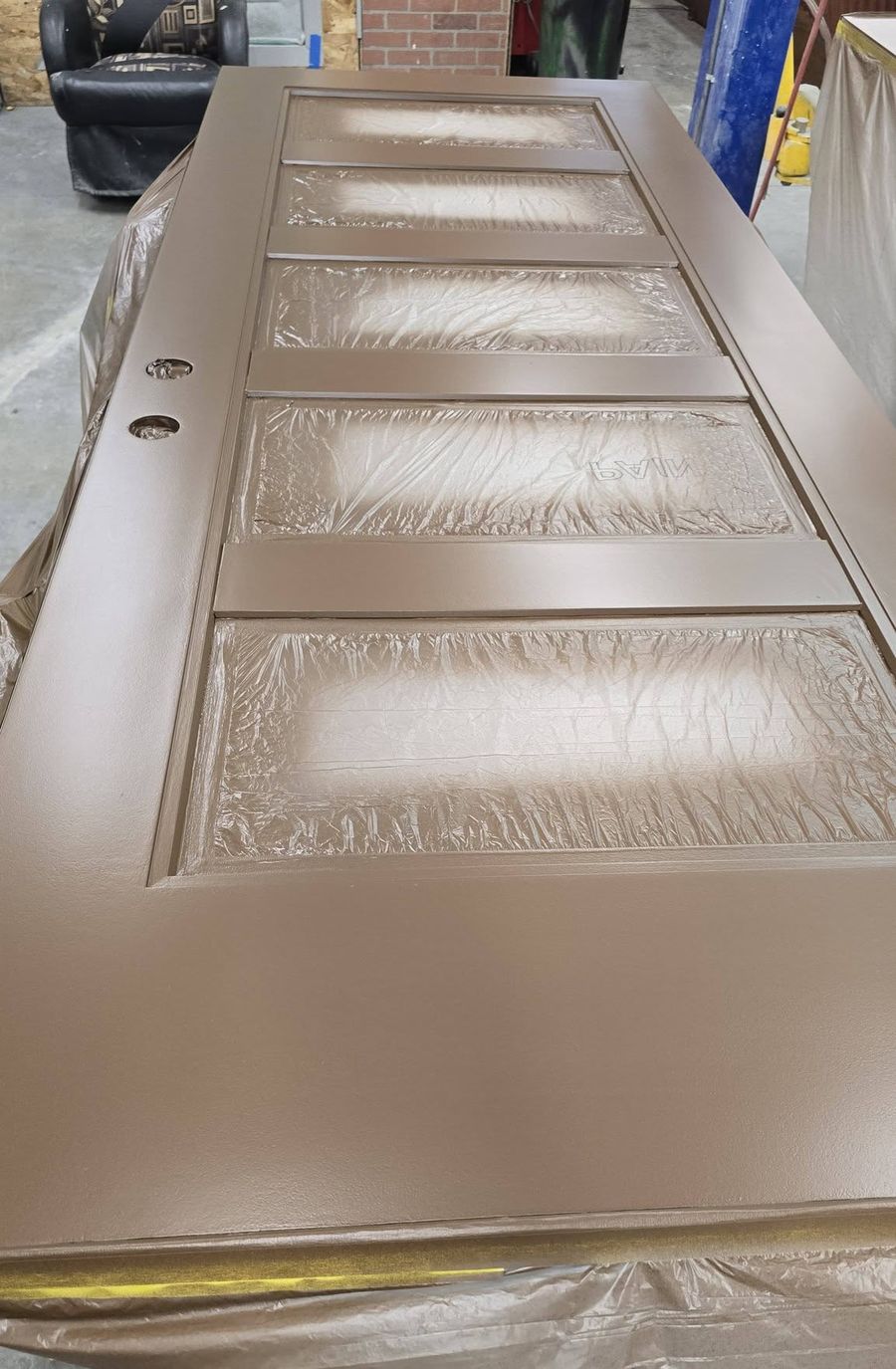 Entry door slab with a fresh brown finish in the shop, glass lites masked off