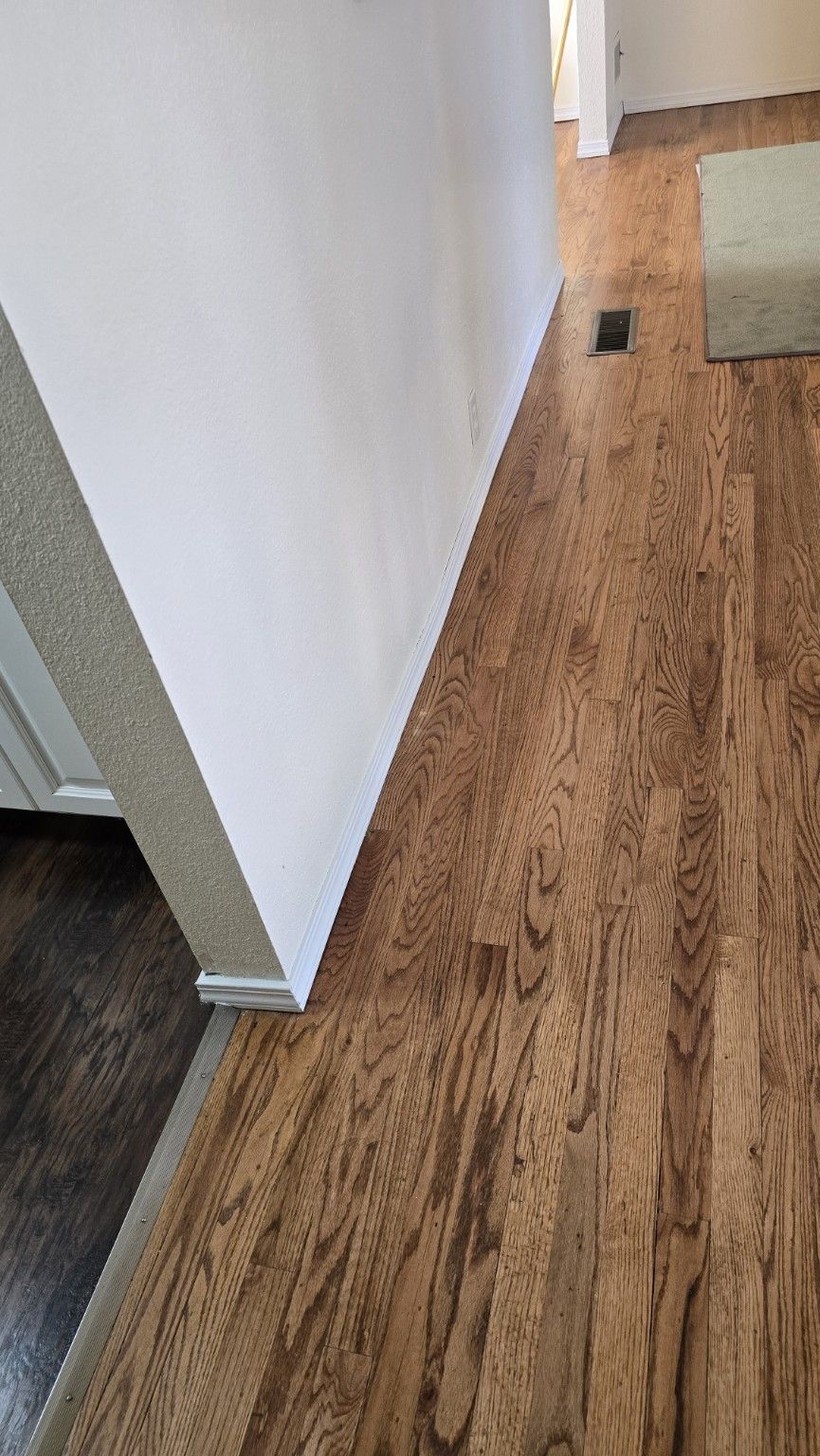 Hardwood hallway floor with fresh white baseboard on a Speedy's flooring job