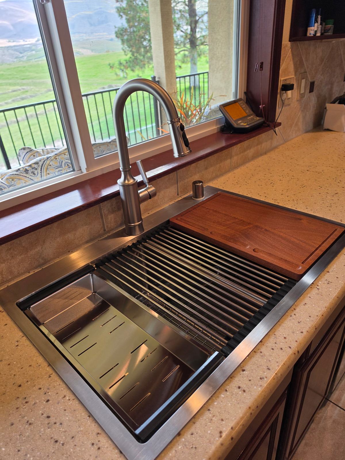 New stainless workstation sink and faucet set in a speckled countertop below a kitchen window, on a Speedy's kitchen sink replacement
