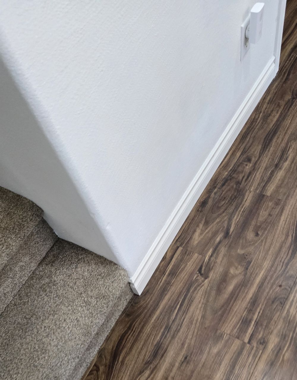 Plank flooring and white baseboard finished along a stair landing