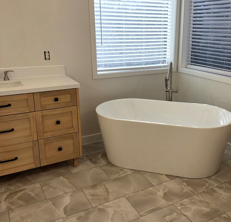 Wood vanity with a quartz top beside the freestanding tub, new tile floor